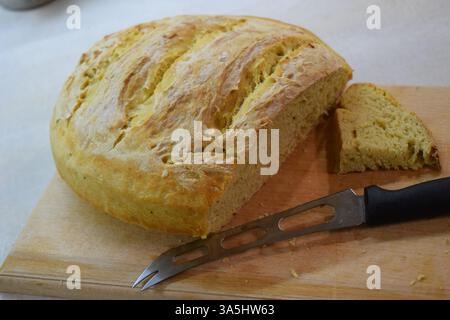 A loaf of freshly baked bread with a golden brown, crispy crust and a soft, fluffy interior, sliced open on a wooden cutting board with a bread knife Stock Photo