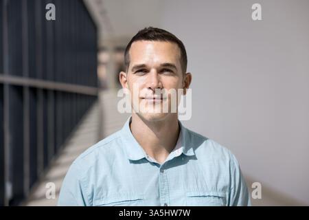 Close up head shot of handsome European businessman, executive manager dressed in casual blue shirt, posing indoors, look at camera, stand in empty of Stock Photo