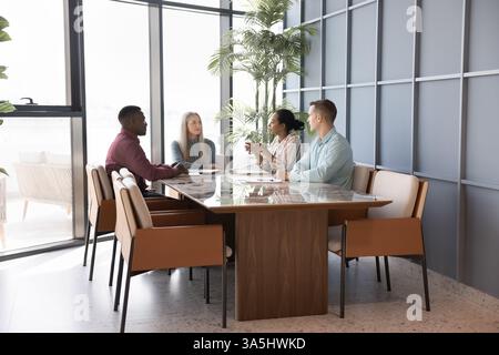 Group of four professionals engaged in meeting in conference room. Young African woman boss, team leader provides explanations, corporate goals and pr Stock Photo