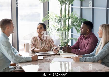 Young African businesswoman, team leader, boss presents ideas or insights to multiethnic group, discussing strategy, sharing project updates, offering Stock Photo