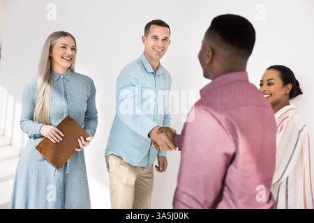 Group of young multiracial teammates met each other in corporate office hallway, two team leaders shaking hands, expressing mutual respect and recogni Stock Photo