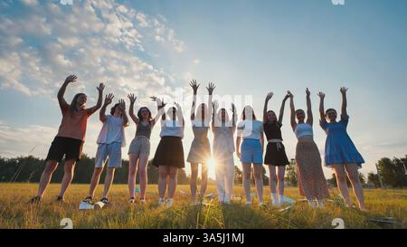 Group of happy students waving goodbye at sunset in a field, celebrating the end of school Stock Photo