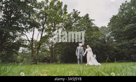 Loving newlyweds walking hand in hand through verdant park, celebrating marriage union Stock Photo