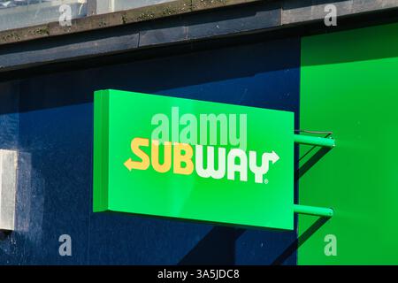 A brightly lit Subway sign is mounted on a dark blue and green building exterior, with the sign's lettering in yellow and white in Manchester, UK. Stock Photo