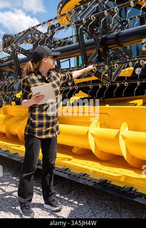 Female farmer using digital tablet standing next to combine harvester at equipment dealership. Stock Photo