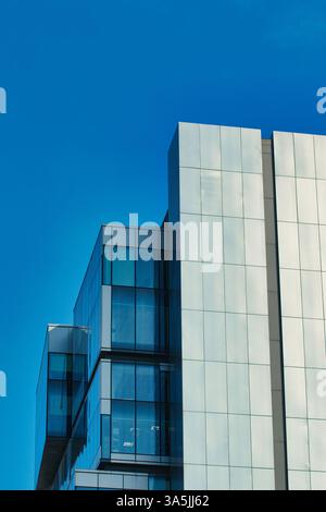 Low-angle shot of a modern building with glass and silver facade under a clear blue sky in Manchester, UK. Stock Photo