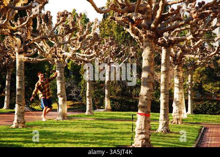 A young man balances himself on a slack rope tied between trees at the University of California Berkeley Stock Photo