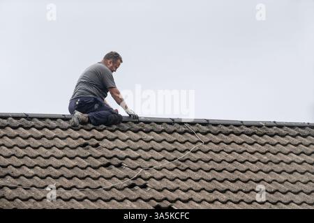 Man sitting aside the apex of a roof repairing ridge tiles Stock Photo