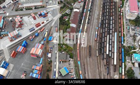 Aerial panorama revealing sprawling freight terminal with parked trains, multicolored containers, bustling transport vehicles Stock Photo