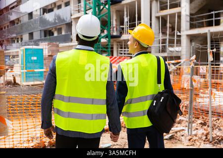 Two architects in protective helmets and jacket look at the unfinished house. View from back Stock Photo