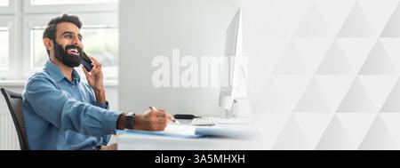 Positive thoughtful indian businessman talking on cellphone and taking notes while working on computer in office Stock Photo