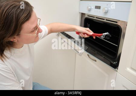 Woman repairing oven with adjustable wrench in kitchen. Home appliance maintenance and repair concept. Stock Photo