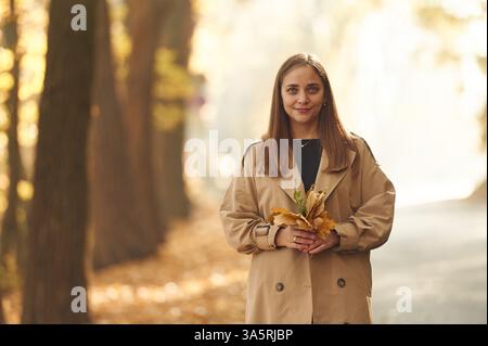 Wellbeing, holding fallen leaves. Happy woman is in the autumn forest. Stock Photo