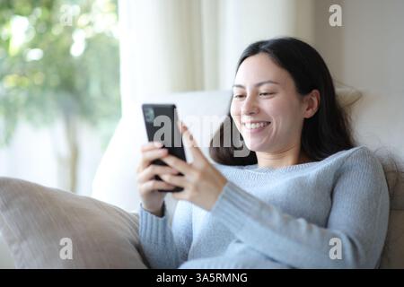 Happy asian woman is using smart phone sitting on a couch at home Stock Photo