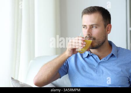 Man drinking orange juice sitting on a couch at home Stock Photo