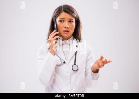 Studio shot portrait of worried female doctor who is talking on phone with patient. Stock Photo
