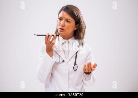 Studio shot portrait of worried female doctor who is talking on phone with patient. Stock Photo