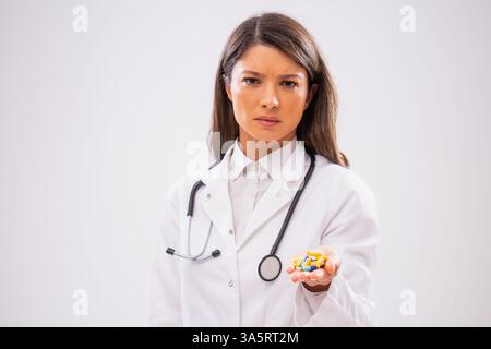 Studio shot portrait of worried female doctor who is holding pills in her hand. Stock Photo