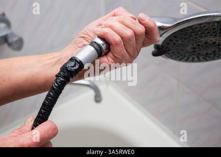 Woman changing broken shower hose in bathroom. Female plumber hands fixing hose. Plumbing concept. Male and female professions concept. Stock Photo