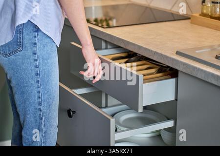 Person opens a kitchen drawer with various utensils in wooden cutlery tray. Woman opening kitchen cabinet. Concept of home organization and functional Stock Photo