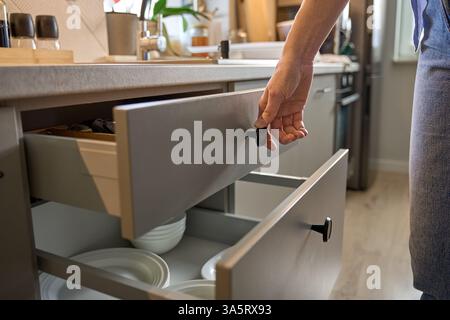 Person opens a kitchen drawer with various utensils in wooden cutlery tray. Woman opening kitchen cabinet. Concept of home organization and functional Stock Photo