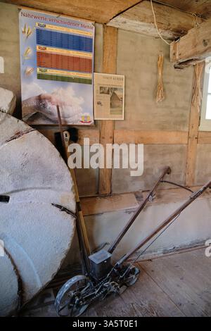 Large segmented peeling stone and sowing machine on display inside a historic mill. The wooden interior features old tools and framed prints, adding a Stock Photo