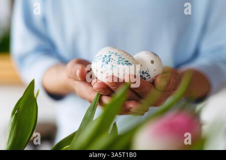 Hands holding decorated Easter eggs with traditional patterns, surrounded by festive spring elements. Stock Photo