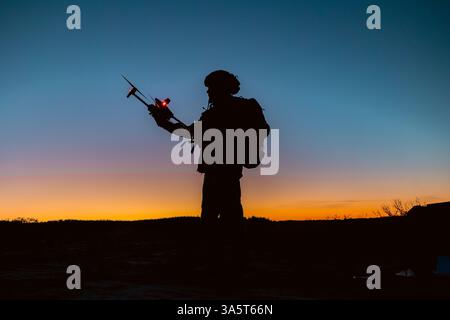 Silhouettes of soldiers are using drone for scouting during military operation against the backdrop of a sunset. Application of modern technology duri Stock Photo