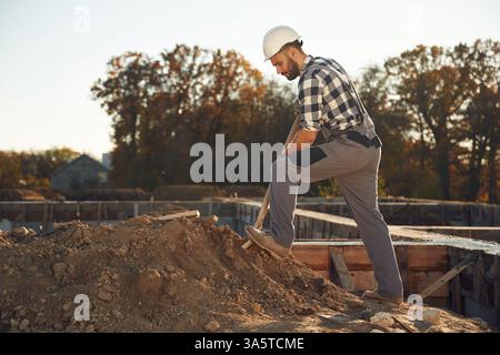Digging, using shovel. Worker is on the construction site at daytime. Stock Photo