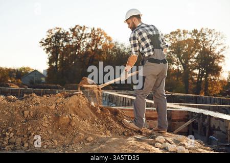 Digging, using shovel. Worker is on the construction site at daytime. Stock Photo