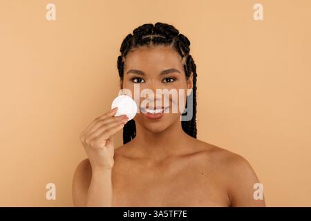 Young woman smiling while holding cotton pad, cleansing skin Stock Photo