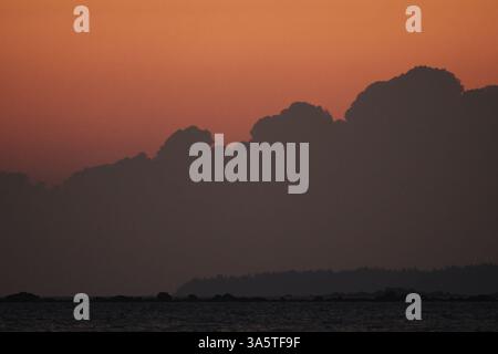 Sunset at the sea with dark clouds rising up in the horizon. Stock Photo