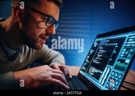 Side view. Male programmer is working indoors by a laptop. Stock Photo