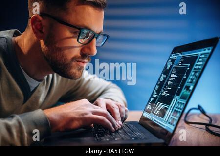 Side view. Male programmer is working indoors by a laptop. Stock Photo