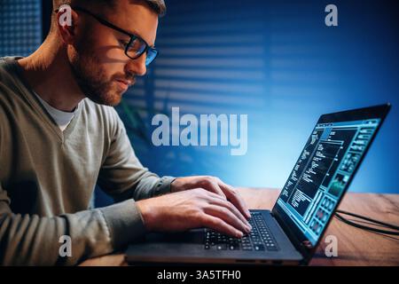 Side view. Male programmer is working indoors by a laptop. Stock Photo