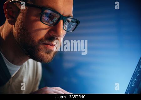 Focused on job. Male programmer is working indoors by a laptop. Stock Photo