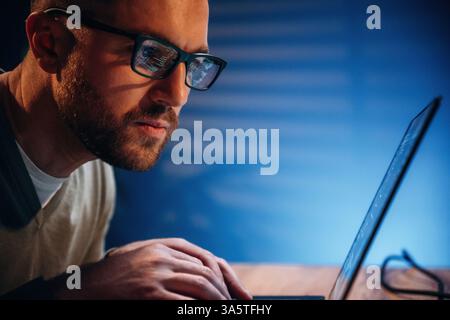 Focused on job. Male programmer is working indoors by a laptop. Stock Photo