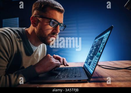 Focused on job. Male programmer is working indoors by a laptop. Stock Photo