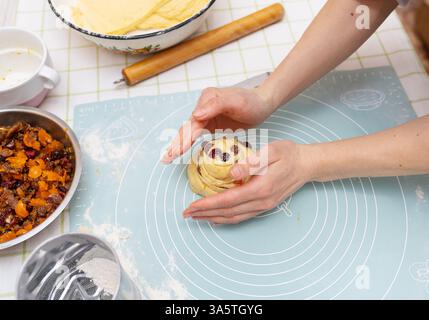 A young Caucasian woman's hands carefully shape a sweet Easter bread roll, filled with dried fruit. The festive pastry is almost ready for baking. Stock Photo