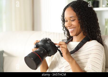 Happy black woman checking dslr camera sitting on a couch at home Stock Photo