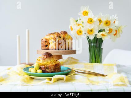 An Easter table displays a sweet bread, pastel eggs, and a daffodil bouquet. The springtime arrangement evokes warmth and celebration, ideal for Easte Stock Photo