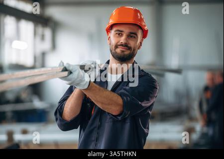 Holding metal pieces, planks. Man is working in the modern factory. Stock Photo