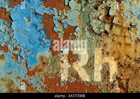 A close-up of a heavily weathered steel surface covered in multiple layers of cracked and peeling paint in shades of blue, brown, and beige. Stock Photo