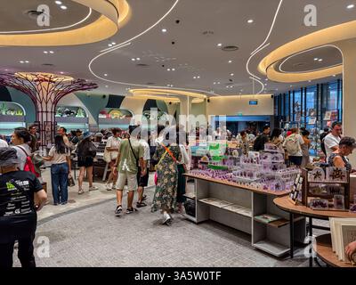 The gift shop in Garden By The Bay is filled with shoppers browsing merchandise. The shop has a modern design with a tree-like sculpture. Stock Photo
