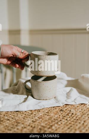 A person is holding two white ceramic coffee mugs. The mugs are placed on a table, and the tablecloth is white. Concept of warmth and comfort, as the Stock Photo