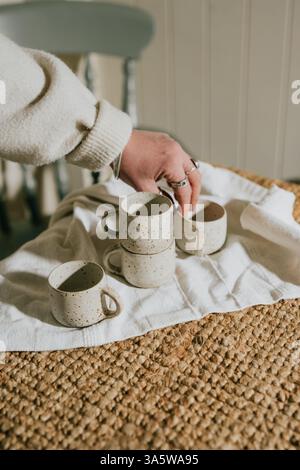 A person is holding four white cups on a table. The cups are arranged in a row and the person is touching one of them. The scene has a casual and rela Stock Photo