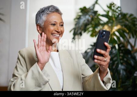 Mature Professional Smiling and Waving During a Video Call on Her Smartphone Stock Photo