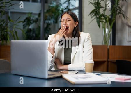 Professional Woman Feeling Tired at Work, Sitting by Her Laptop in a Modern Office Stock Photo