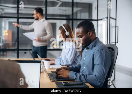 Focused, sitting by laptop. Professional workers are in the modern office together. Stock Photo