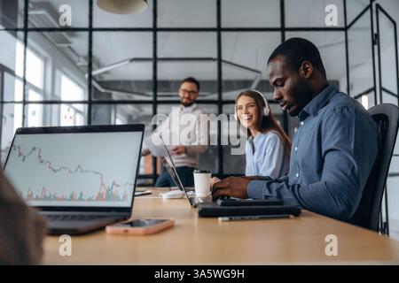Focused, sitting by laptop. Professional workers are in the modern office together. Stock Photo